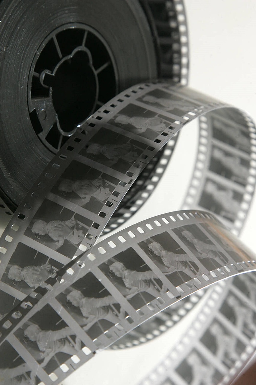 A close-up of a reel of photographic film, unwound and curving, displays multiple frames with black-and-white images of a standing person—each capturing a different pose, evoking the feeling of Imposter Syndrome.