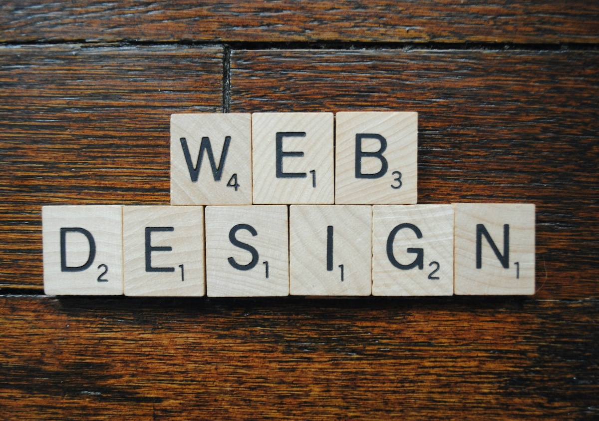 Scrabble tiles arranged on a wooden surface spell out WEB DESIGN, with WEB on the top row and DESIGN below it.