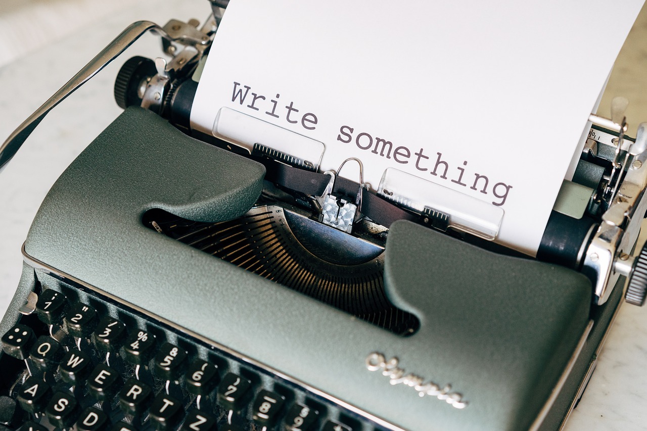A vintage typewriter with a sheet of paper that reads “Write something” in large typewriter font. The visible keys and levers evoke classic writing, capturing the spirit of creativity and The Certainty of Chance.